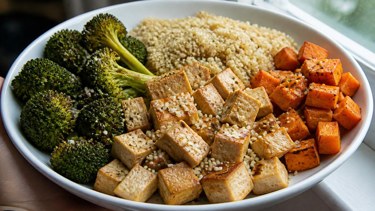 Close-up of a prepared vegan meal plate with firm tofu cubes, fluffy quinoa, roasted broccoli and sweet potato, hemp seeds sprinkled on top, natural window lighting showing portion sizes