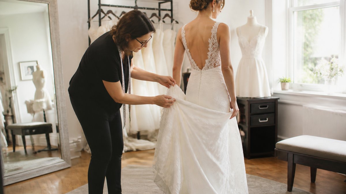 Professional demonstrating how to bustle a wedding dress step by step technique in modern clinical setting with natural lighting