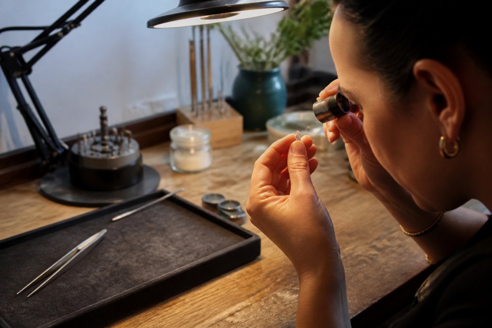 Jeweler using a loupe to inspect the facets of antique diamond earrings on a velvet tray under a desk lamp