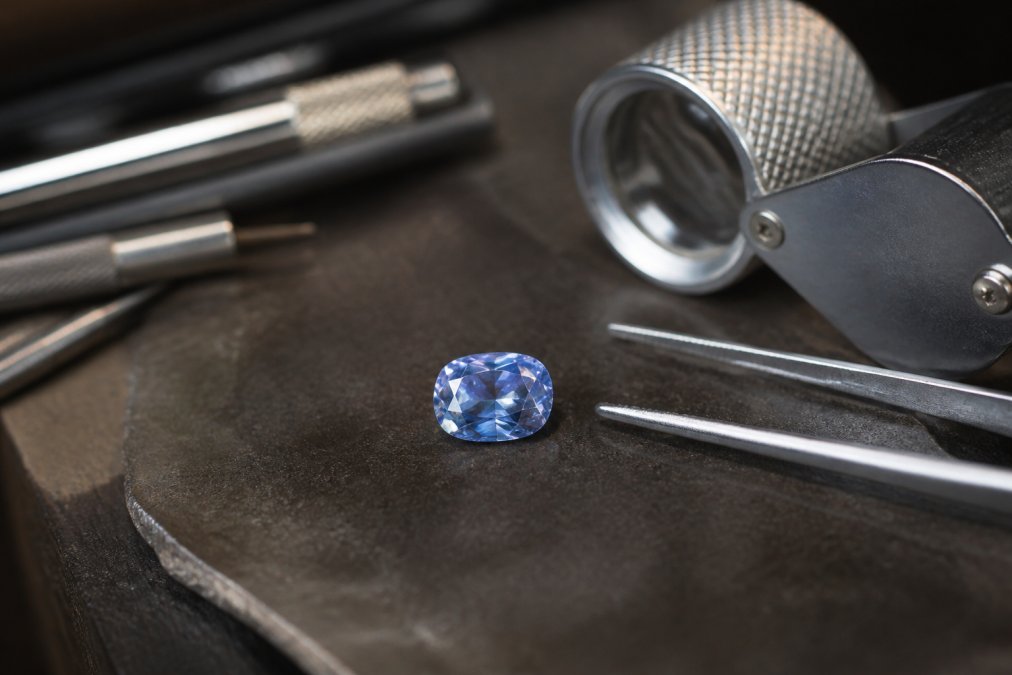 Close-up of a luxury gemstone under professional lighting showing intricate faceting and clarity, displayed on a jeweler's work surface with precision tools