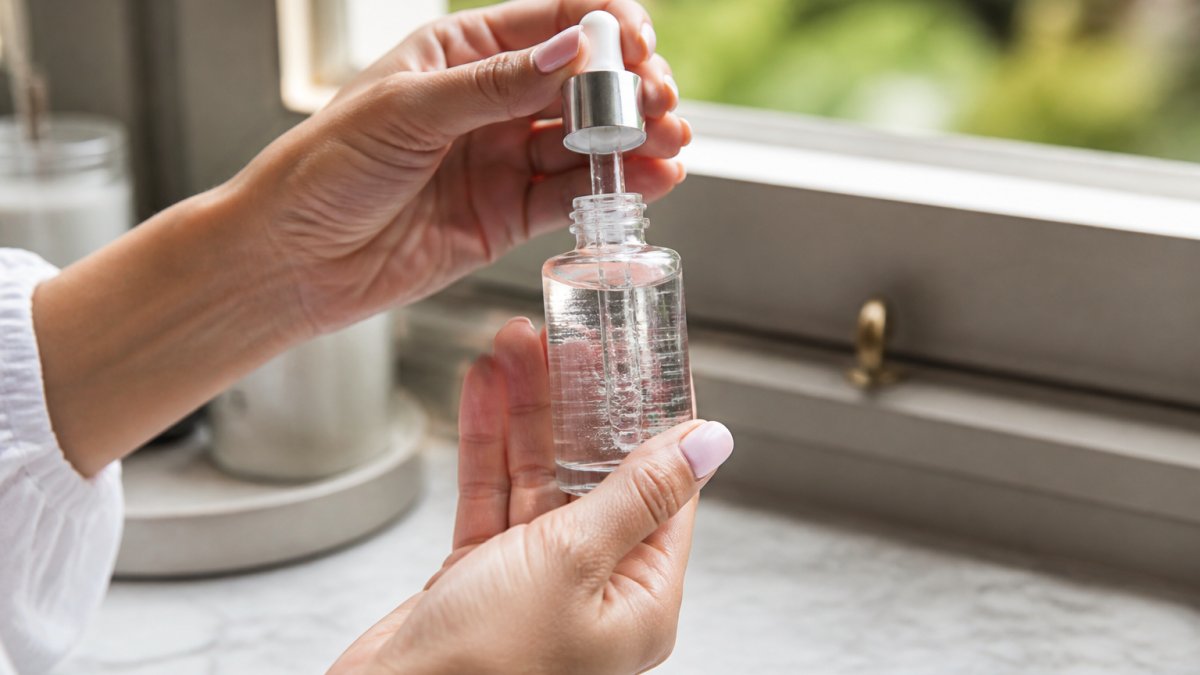 Close-up of hands holding a clear serum bottle with visible concentration label against natural window light