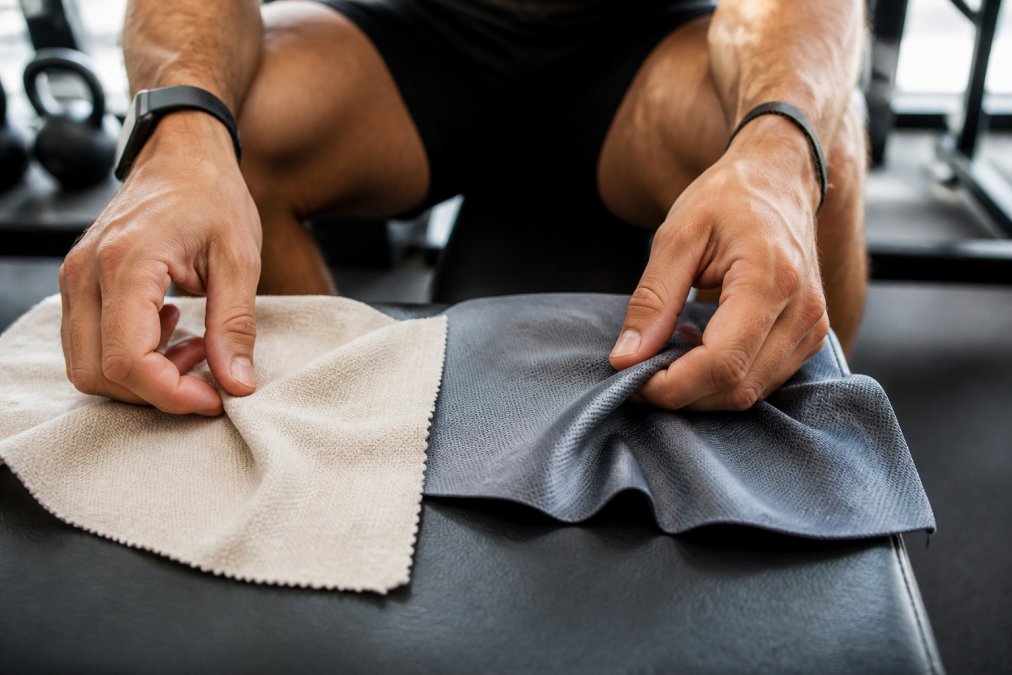 Close-up of an athlete's hands feeling the texture of two fabric swatches, one soft organic cotton and one smooth recycled polyester, in a bright gym setting