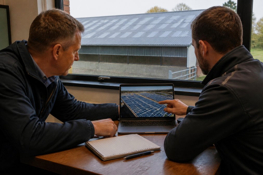 Business owner and consultant reviewing commercial solar ROI data inside a rural farm office with shed visible