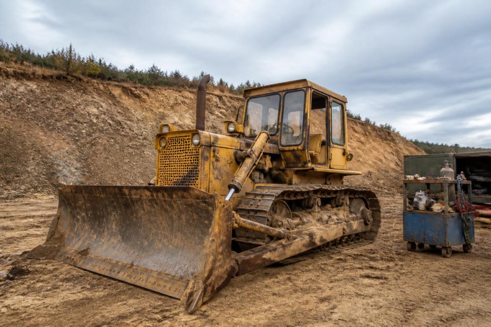 Used bulldozer on construction site showing visible wear and weathering, with maintenance equipment visible nearby
