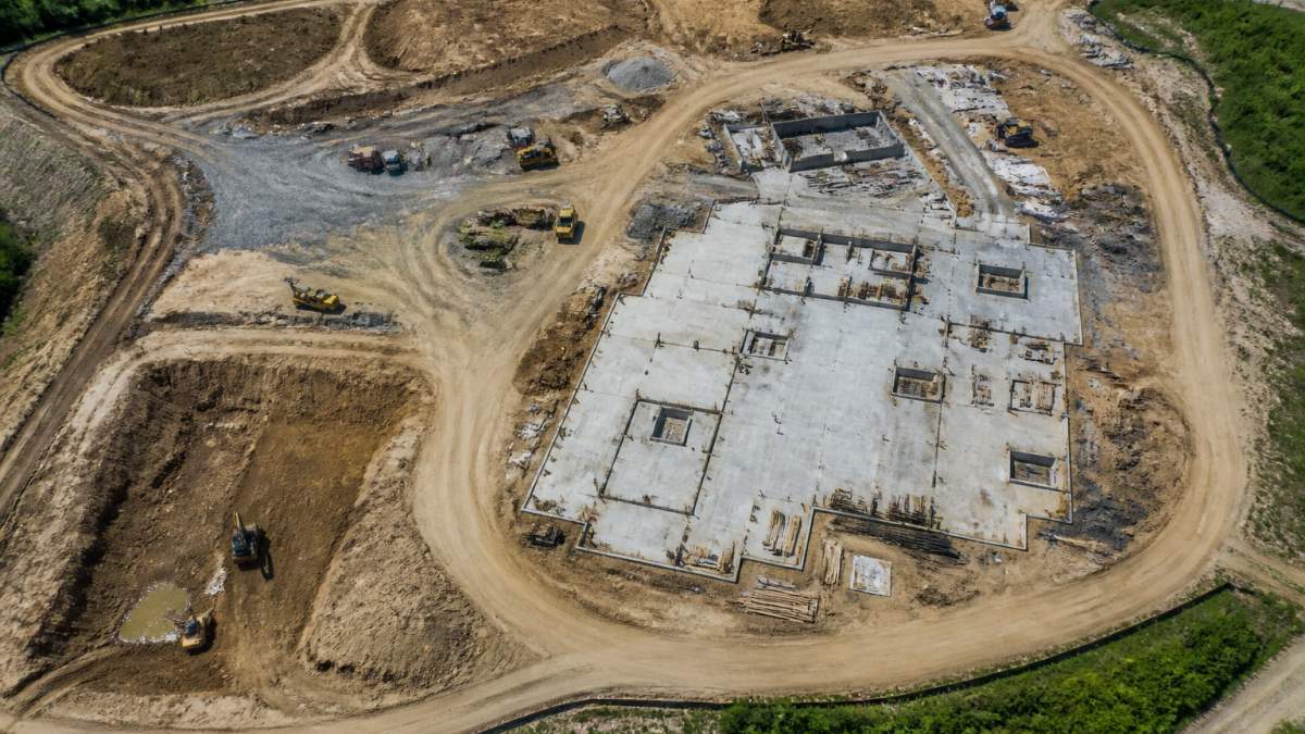 Aerial view of a construction site showing equipment, building foundations, and varied terrain with clear site boundaries visible from above