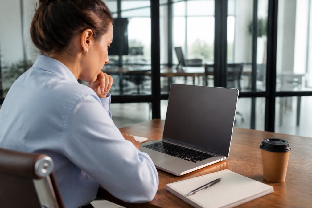 Marketing professional reviewing influencer campaign analytics on laptop screen with notebook and pen, focused on social media performance data in bright office setting