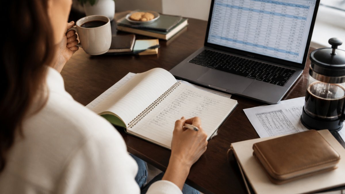 Person working at a home desk with coffee and a budgeting spreadsheet