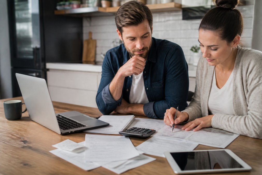 Real estate investor working at desk with laptop, spreadsheet visible on screen, documents and calculator nearby
