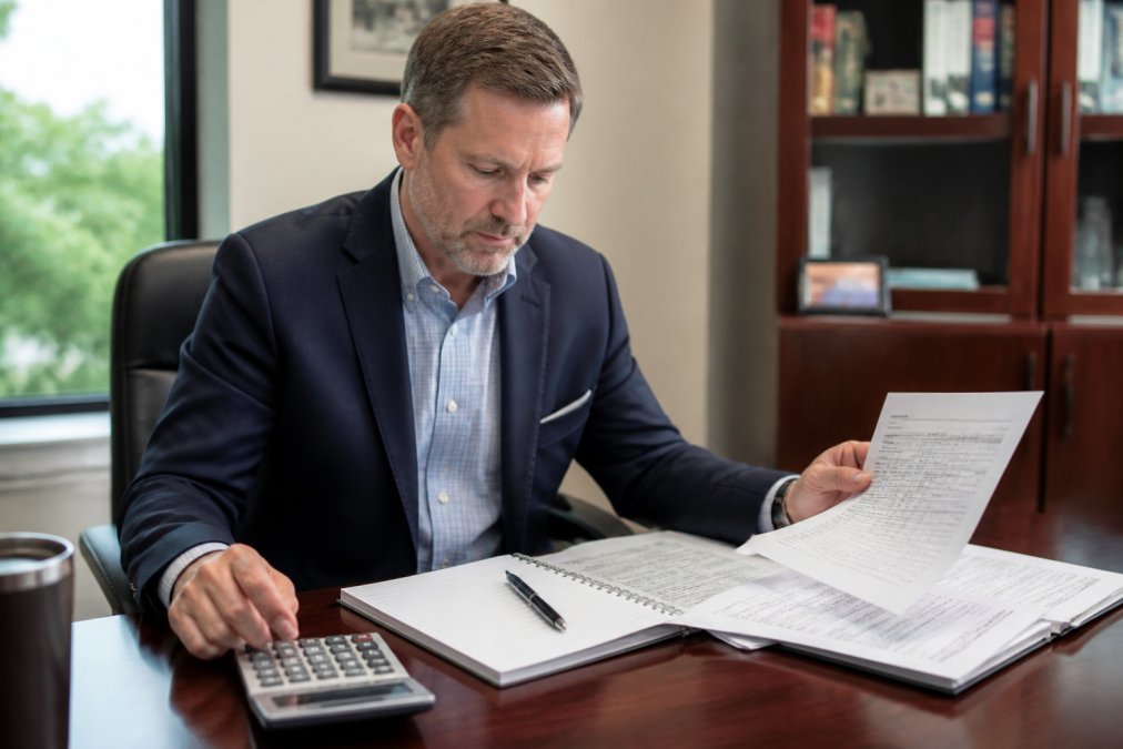 Financial advisor reviewing retirement account statements and tax documents at a desk with calculator and notepad, natural office lighting