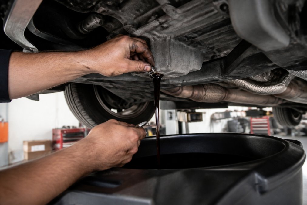 Mechanic removing the drain plug to change Audi oil into a catch pan