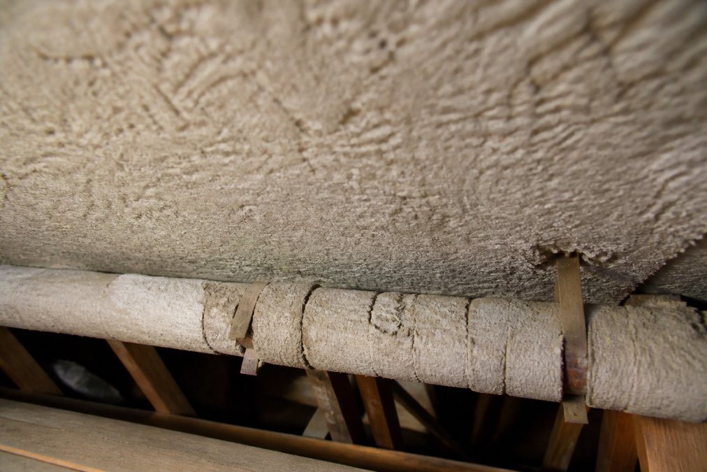 Close-up of an older home's textured ceiling and pipe lagging in a loft, showing potential asbestos-containing materials in situ