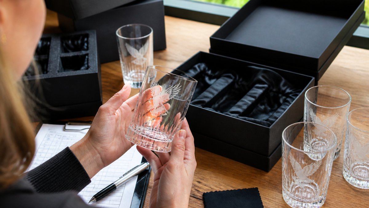 Close-up of hands examining a branded glass sample under natural light, carefully checking print clarity, ink adhesion, and surface finish details