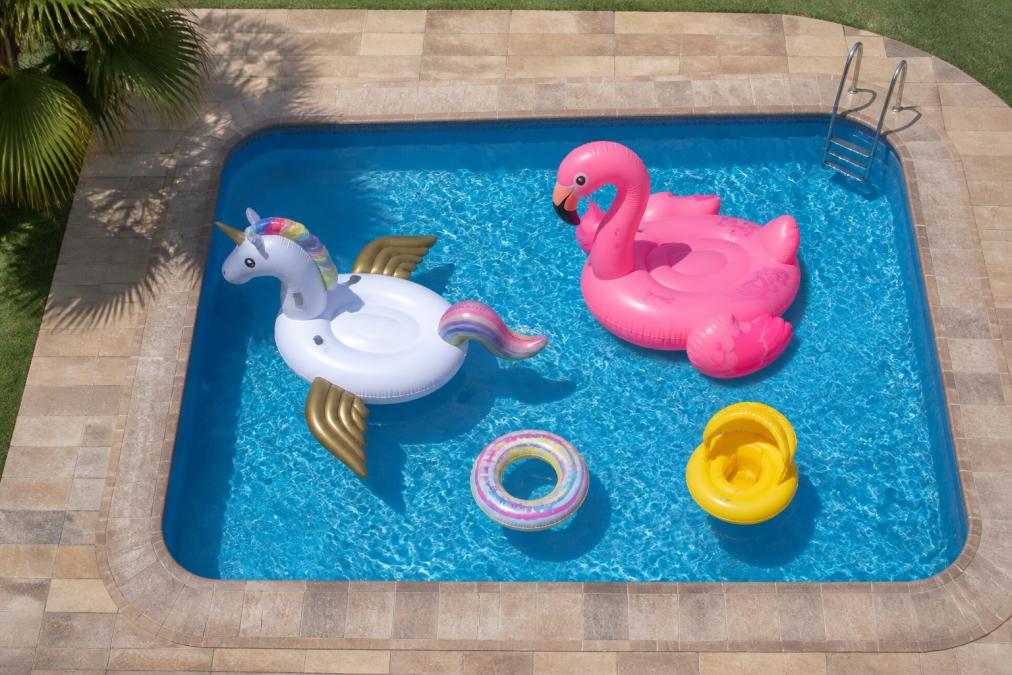 Overhead view of a backyard pool with two large inflatable pool floats and two smaller kids' inflatables floating, showing how much deck and water space they occupy