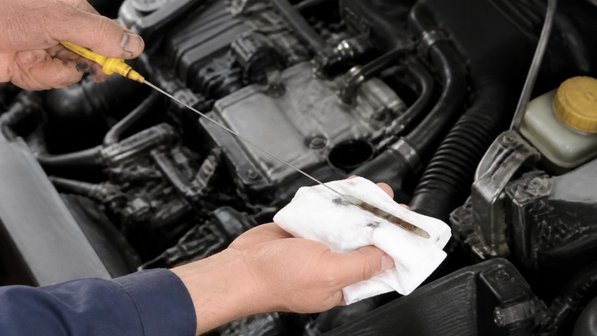Mechanic's hands checking the engine oil dipstick on a used car engine, showing the fluid level clearly against the bright yellow dipstick markings