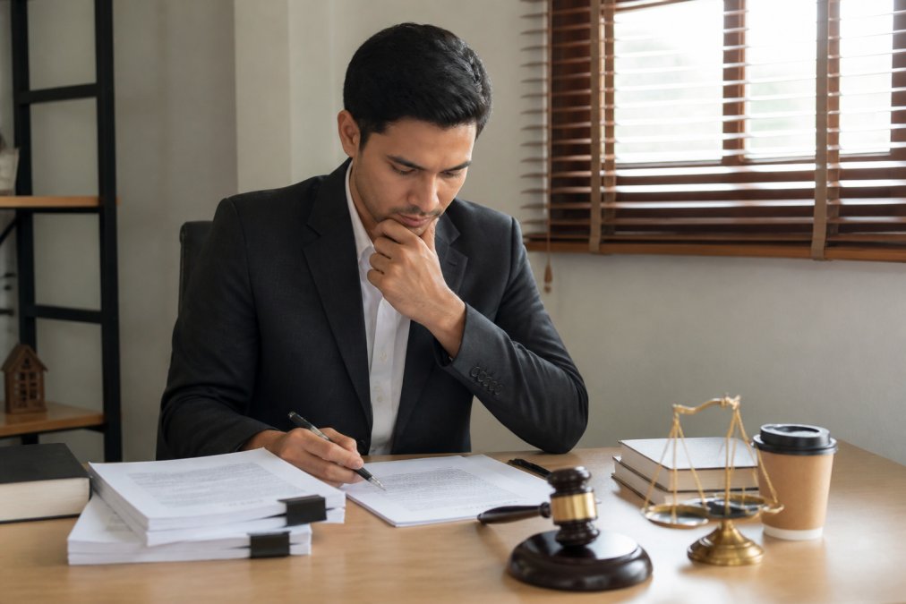 Business owner sitting at desk reviewing legal documents and making notes, with laptop and coffee nearby, appearing thoughtful about business structure decisions