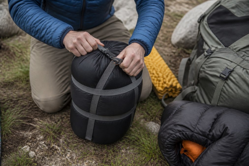 Close-up of hands packing a sleeping bag into a compression sack, demonstrating the compression process and final packed size