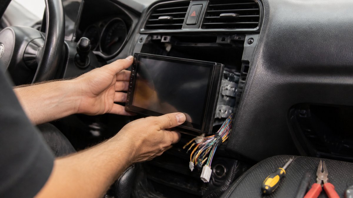 Technician installing a modern touchscreen custom auto radio into a vehicle dashboard in a workshop
