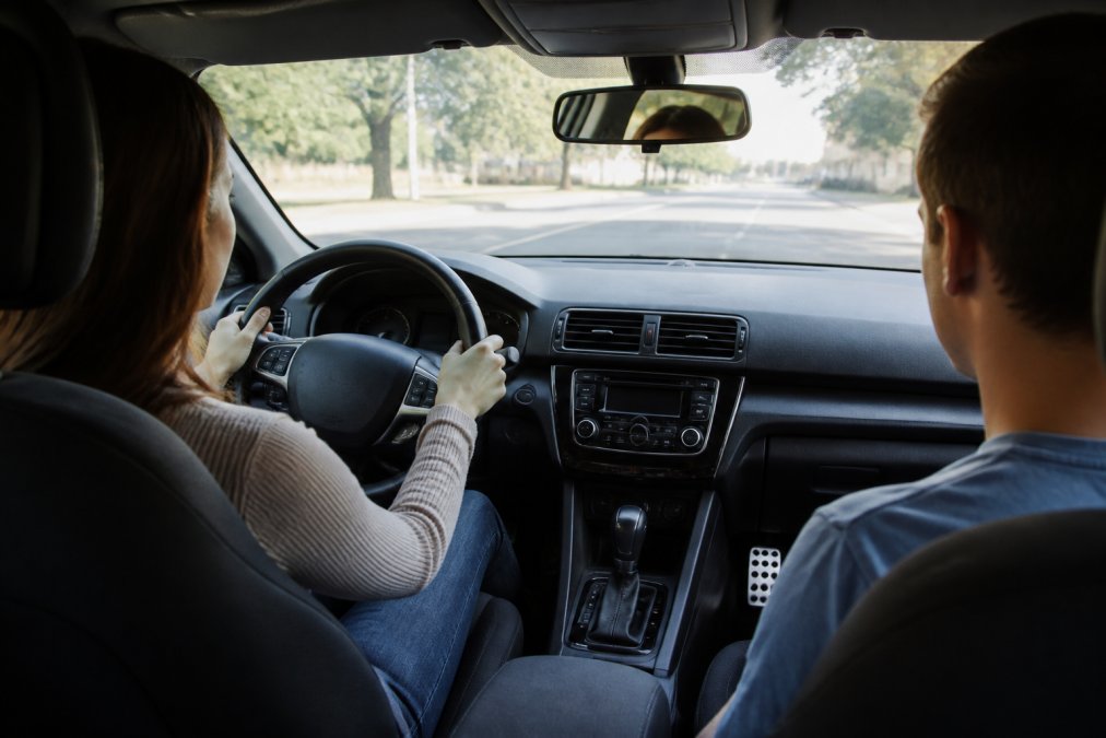A modern dual-control training vehicle with visible backup camera, lane-departure warning indicators on the dashboard, and a passenger-side brake pedal clearly visible