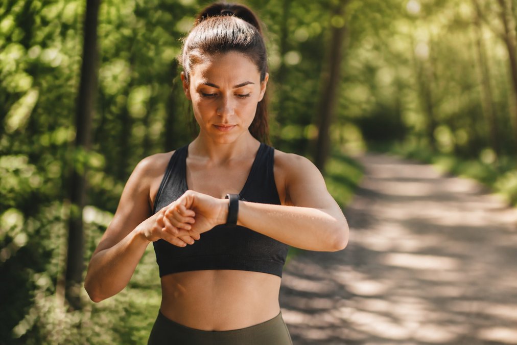 Person wearing a fitness tracker on their wrist while reviewing health metrics on their smartphone during a morning workout session
