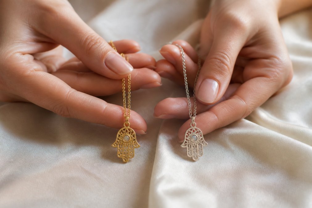 Woman holding a gold plated and sterling silver hamsa hand necklace on soft fabric