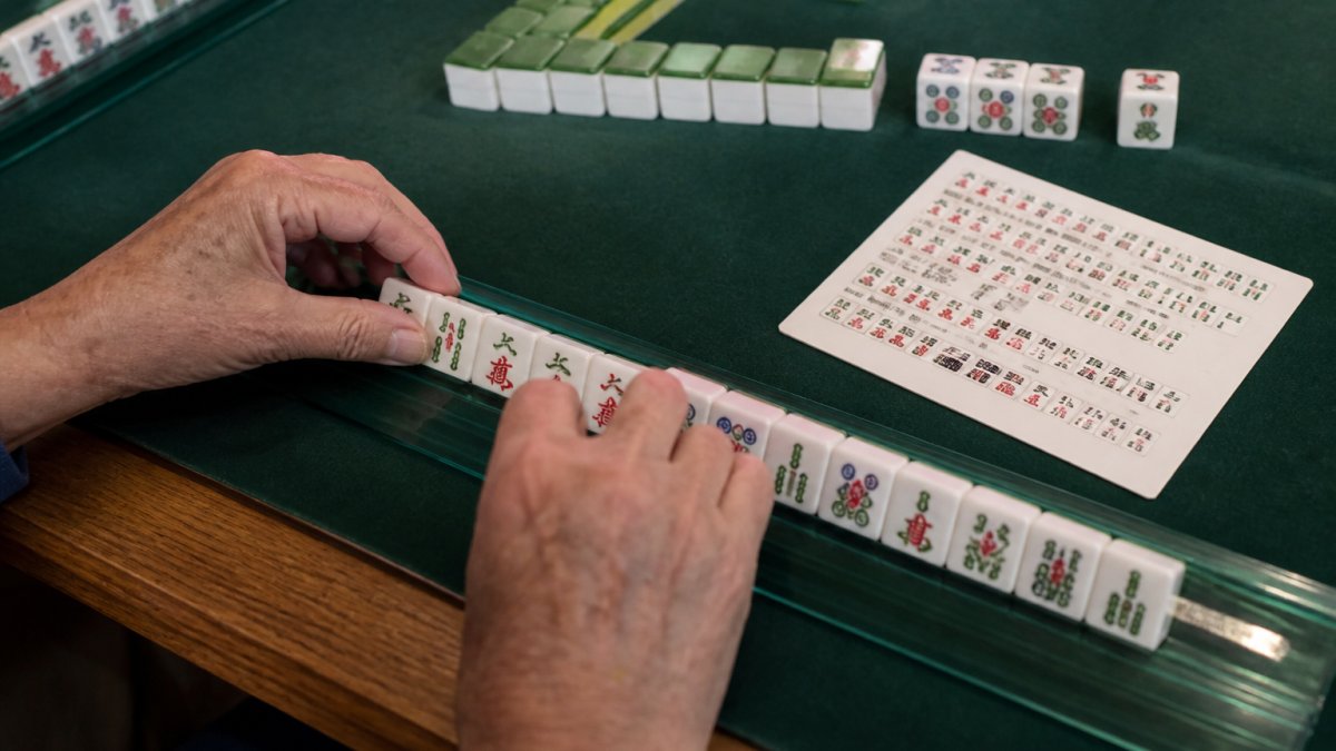 Overhead view of tiles arranged on a rack next to a hand reference card for evaluating a mahjong strategy