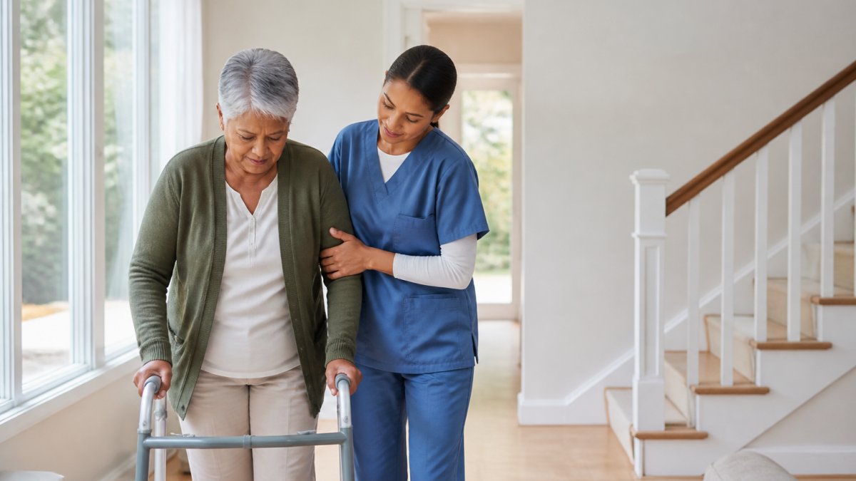 Professional caregiver assisting elderly patient with mobility and balance during home recovery, hands-on support in bright home setting with natural light
