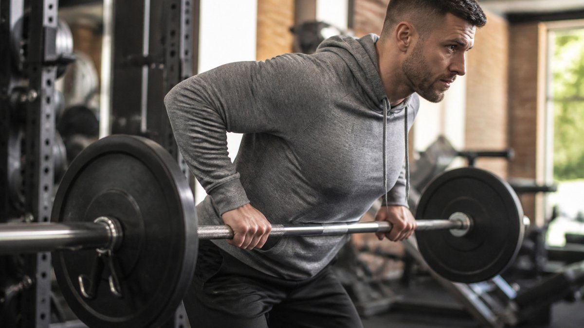 Lifter wearing a heather grey fitted hoodie performing a barbell row in a bright gym setting