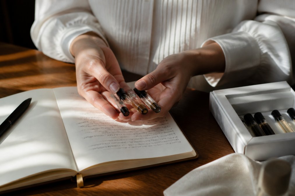 Hands holding perfume sample vials and a notebook of notes to choose a meaningful fragrance for a loved one.