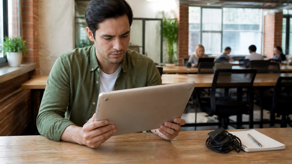 Startup founder inspecting a used silver laptop on a wooden desk in a bright shared office space