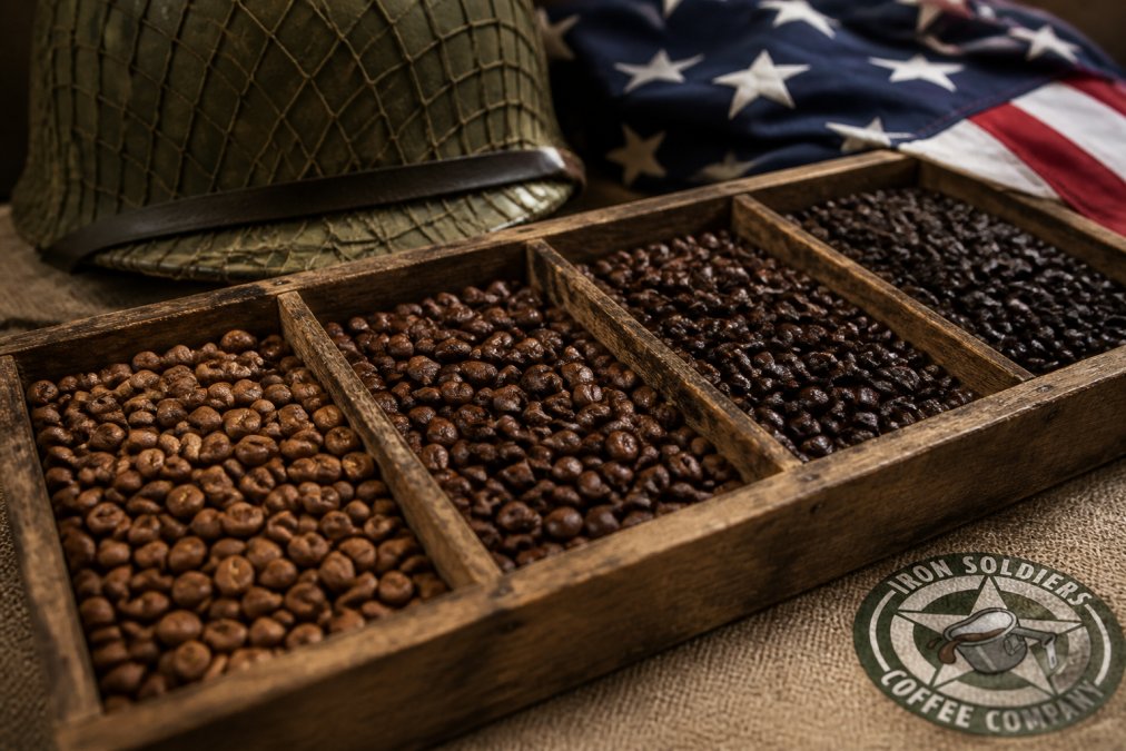 Close-up of freshly roasted coffee beans in various shades of brown arranged in a rustic wooden tray, with a vintage military helmet and a folded American flag in the background under warm natural light