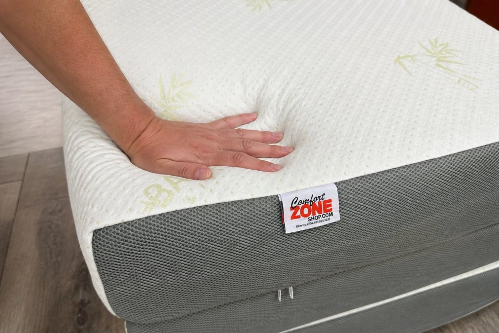 Close-up of a hand pressing into different mattress foam layers, showing memory foam compression and rebound with visible density differences