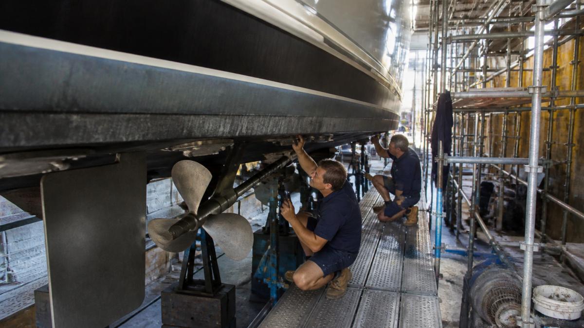 Marine engineers inspect a motor yacht hull at a yacht refit shipyard during a dry dock maintenance project.