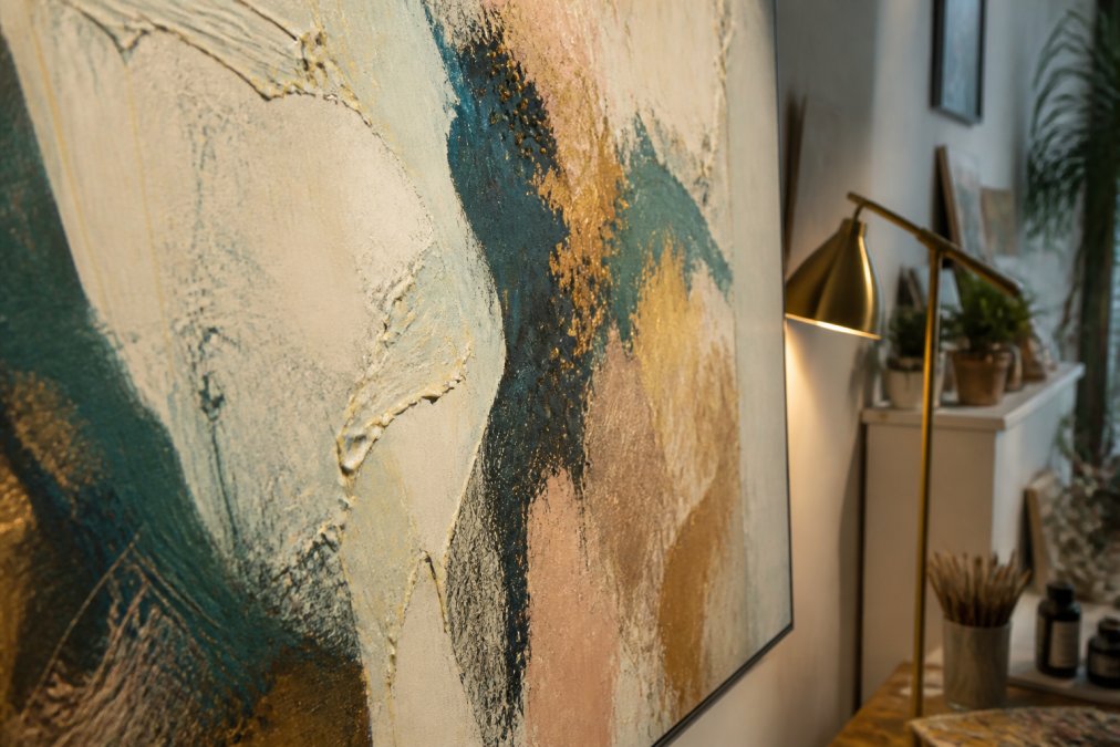 Close-up detail of textured abstract canvas with layered brushstrokes in organic forms, mixed media elements, and varied surface depths, illuminated by warm accent lighting that highlights the artwork's dimensional quality and rich color variations