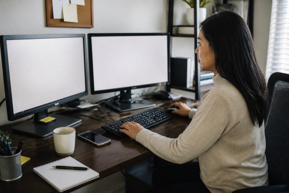 Remote team member working at desk with CRM software open on multiple monitors, managing customer contact information and sales pipeline data with focused concentration