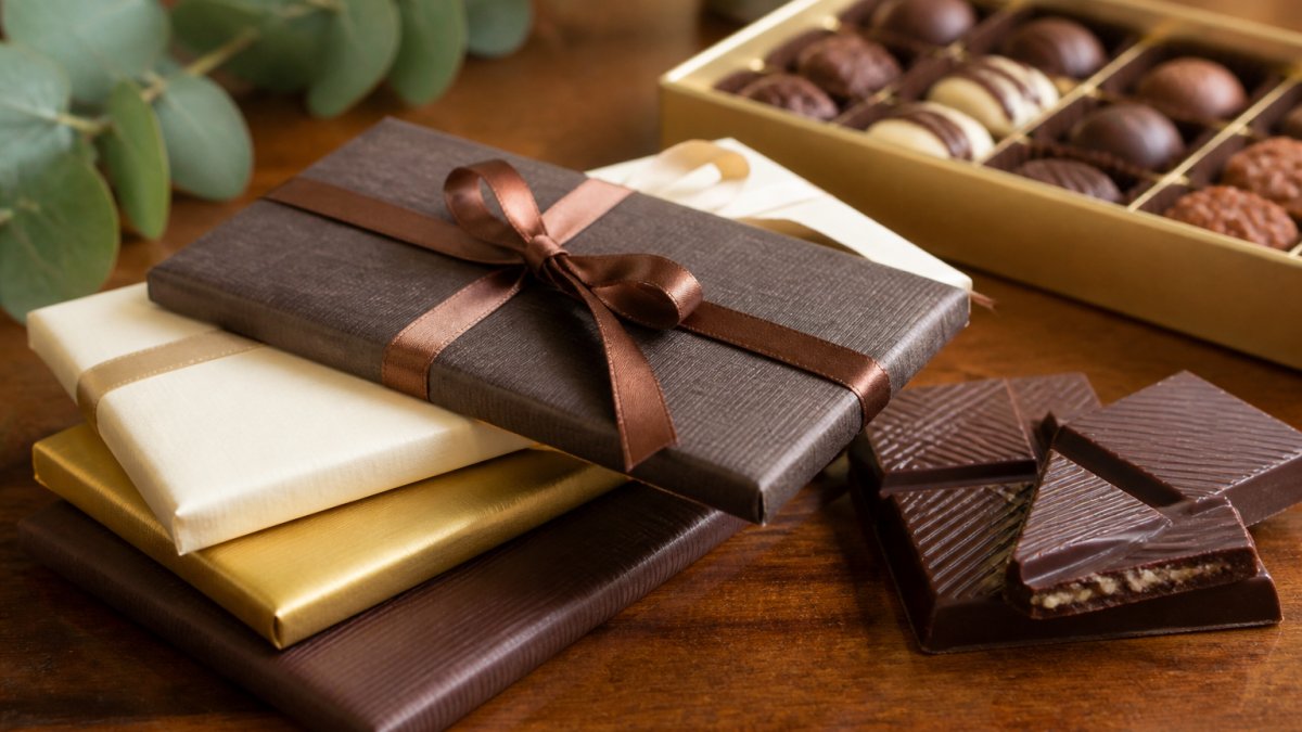 Close-up of elegantly wrapped artisanal chocolate bars with premium packaging displayed on a polished wooden surface with soft natural lighting, showing refined presentation suitable for corporate gifting