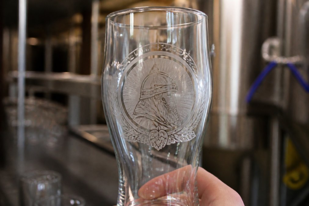 Close-up of a custom beer glass showing intricate laser-engraved logo detail with light reflecting off the frosted etched surface, revealing precise line work and design clarity
