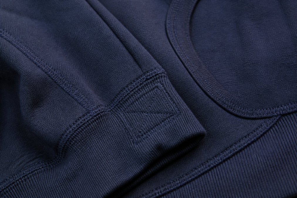 Close-up of reinforced double-stitched seams on navy hoodie fabric showing high stitch density and box-stitch pattern at stress points under natural lighting