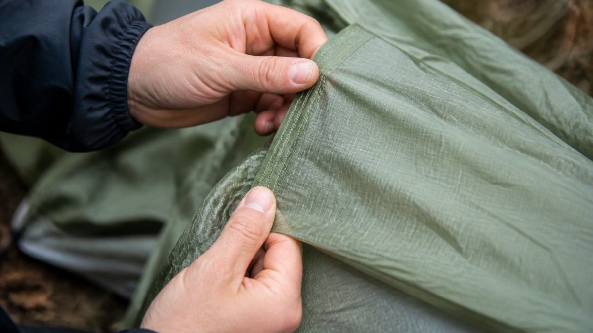 Close-up of hands examining tent seams and fabric, checking stitching quality and water-resistant coating on ripstop material