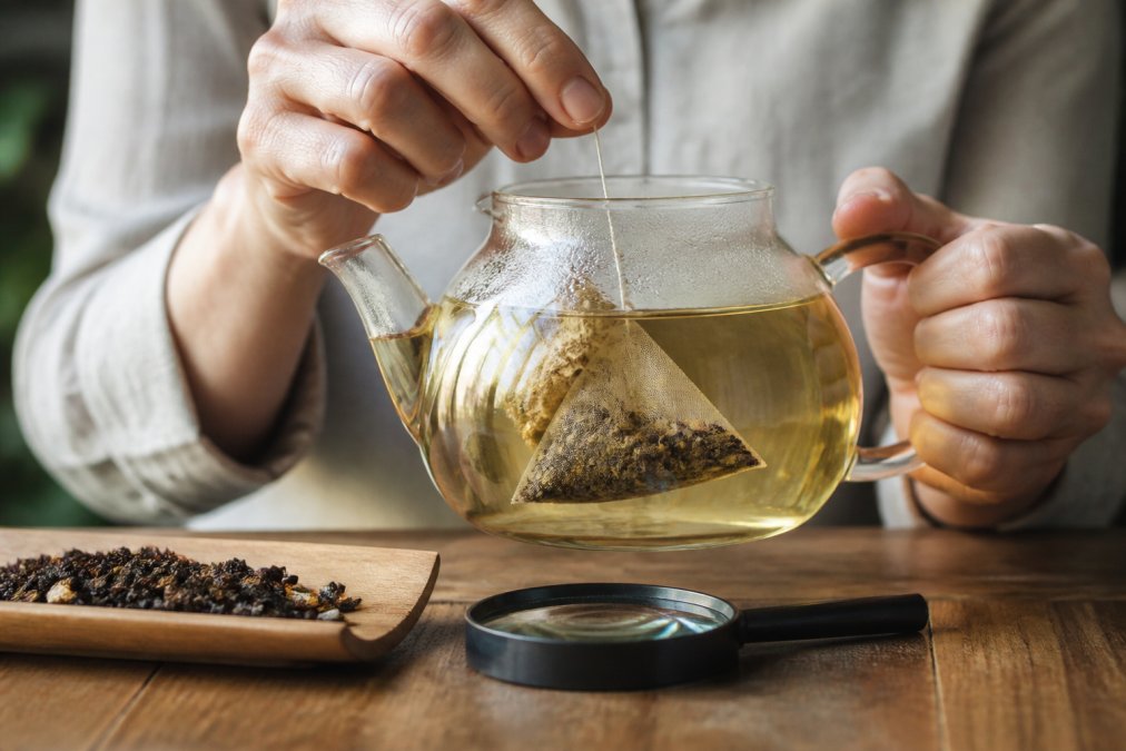 Infographic showing the process of inspecting a pyramid tea bag with a magnifying glass to identify plastic material.