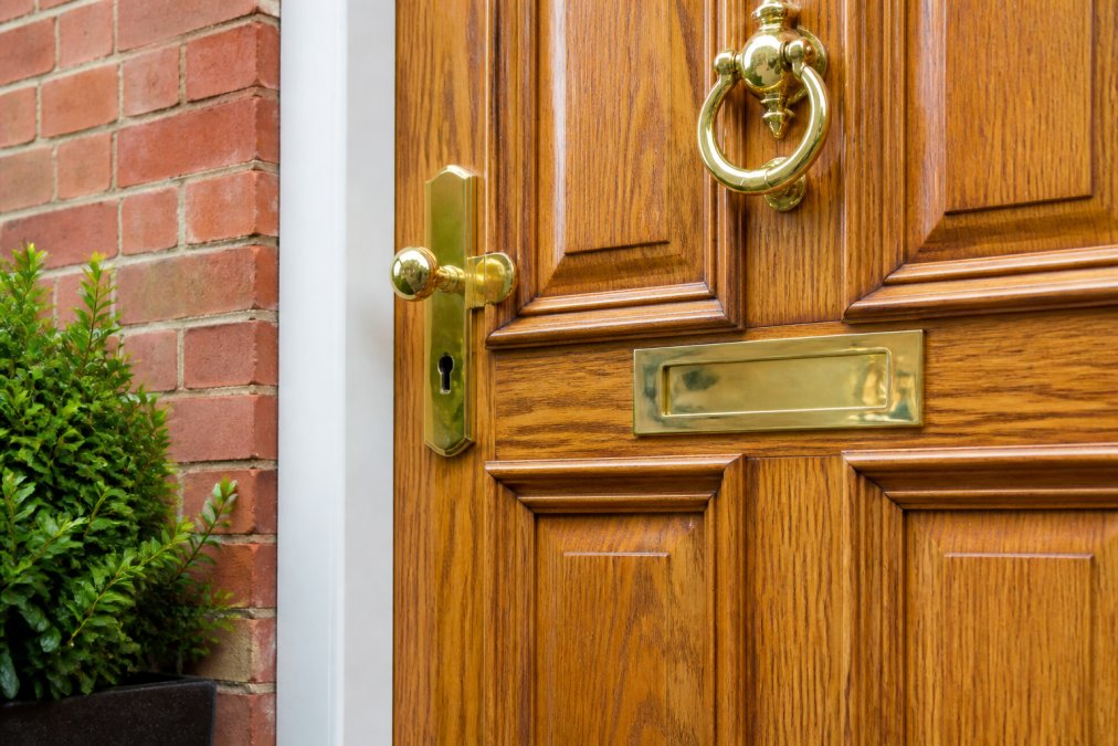 Close-up of a traditional timber front door with raised panelling and polished brass hardware on a period property exterior, showing natural wood grain and finish detail