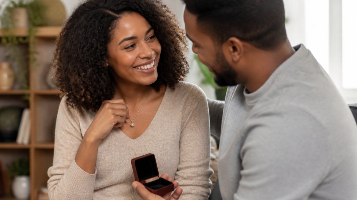 Couple exchanging a personalized necklace or jewelry gift, smiling warmly with genuine emotion, in a cozy home setting with soft natural lighting