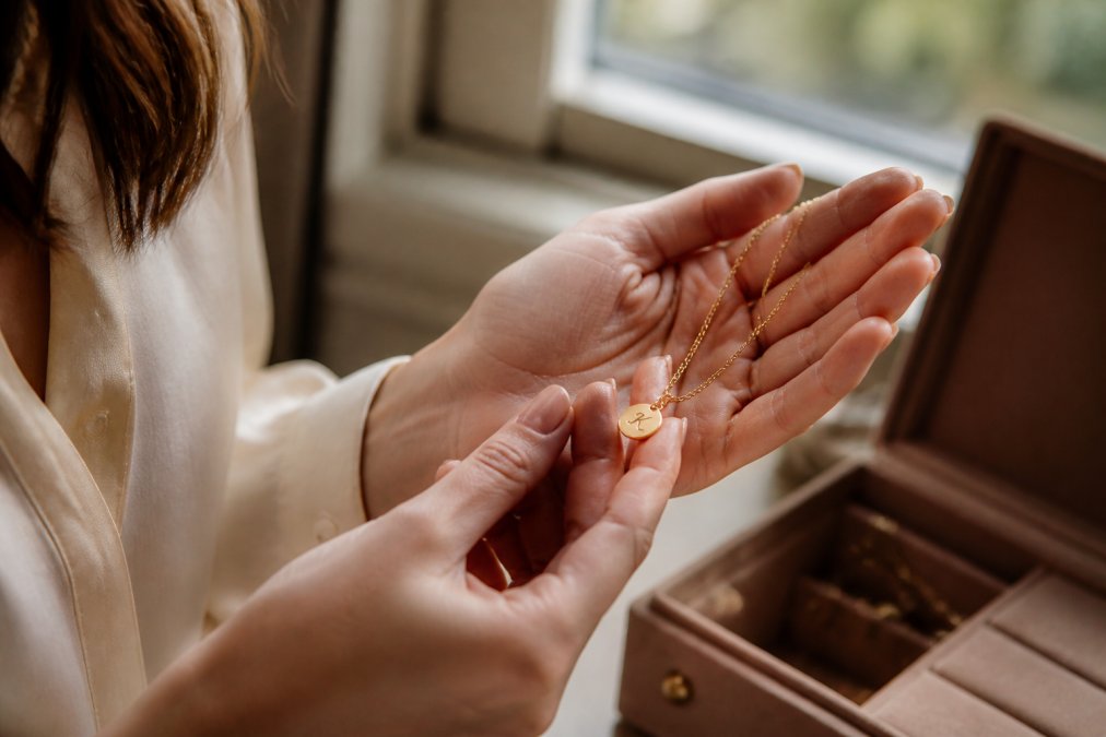 Close-up of a woman's hands holding a delicate gold necklace with an engraved initial pendant, soft natural light, warm and sentimental mood