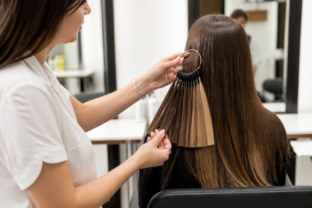 Stylist using a color ring to match premium hair extensions to a client’s natural hair texture and shade.