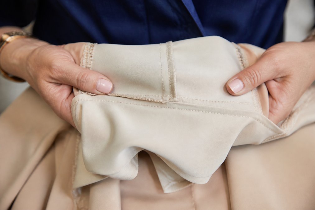 Close-up of hands carefully turning a designer dress inside out to inspect seam stitching and stitch density, showing reinforced seams and neat thread work on the interior construction