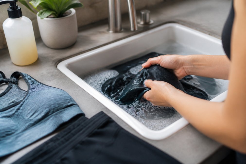 Person carefully hand-washing performance workout apparel in a sink with cool water and gentle detergent, demonstrating proper care technique with delicate handling
