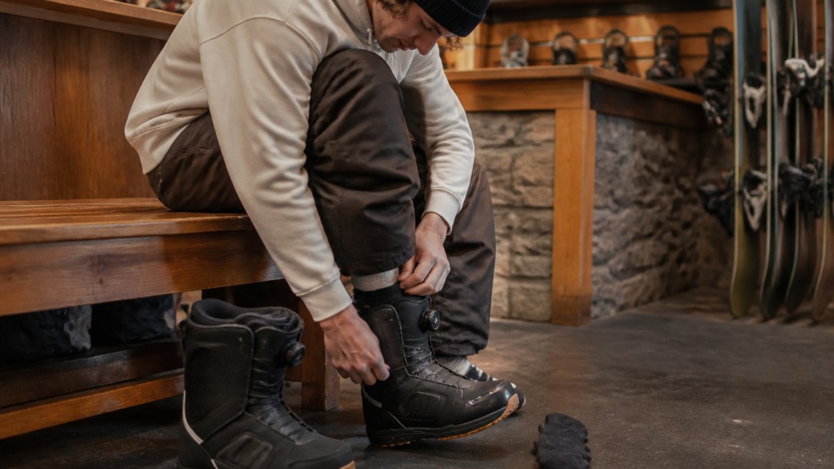 Snowboarder testing boot fit for heel lift in a ski lodge to help choose snowboard gear properly.