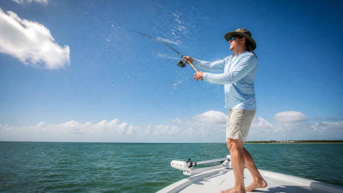 Angler in a long-sleeve performance shirt and hat casting from a boat under bright sun with visible salt spray