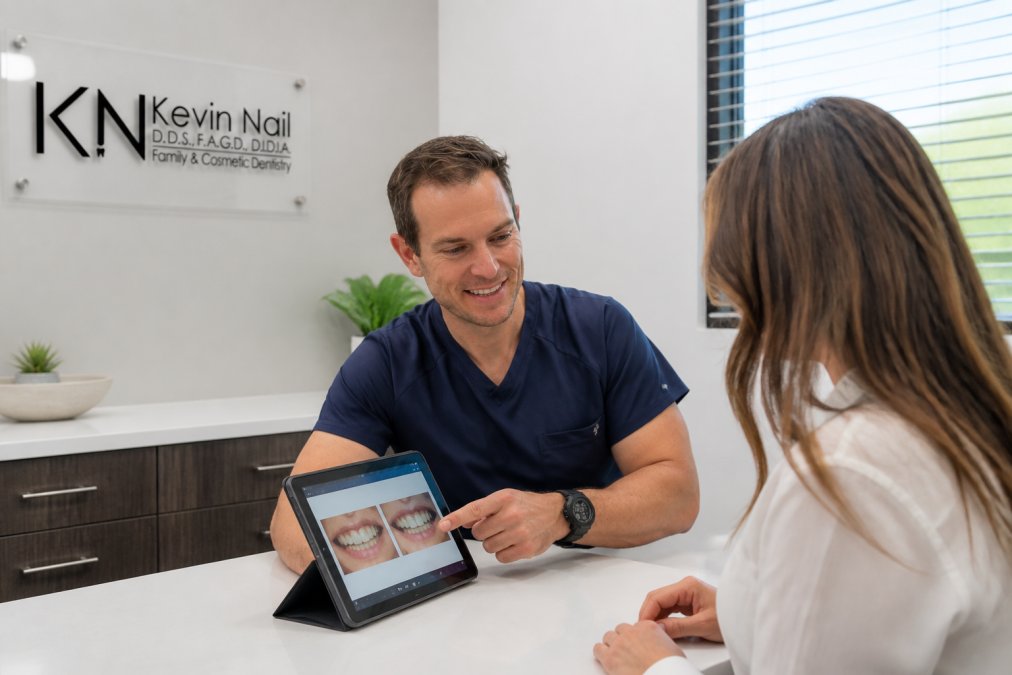 A patient sitting across from a dentist at a consultation desk, both looking at a tablet showing dental treatment plan options, in a clean modern dental office setting