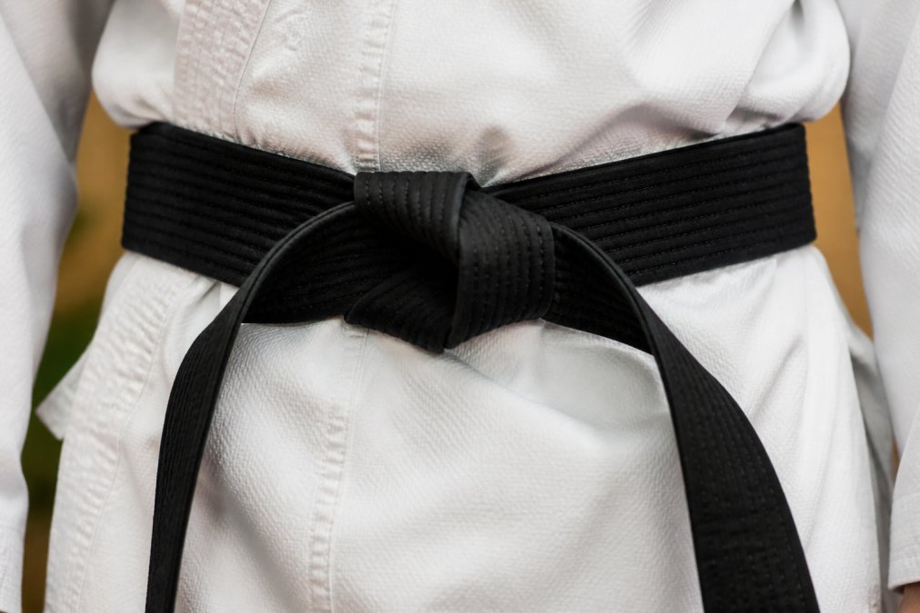 Close-up of a martial arts belt tied around a person's waist, showing the center hole alignment and proper fastening with the belt tongue positioned correctly