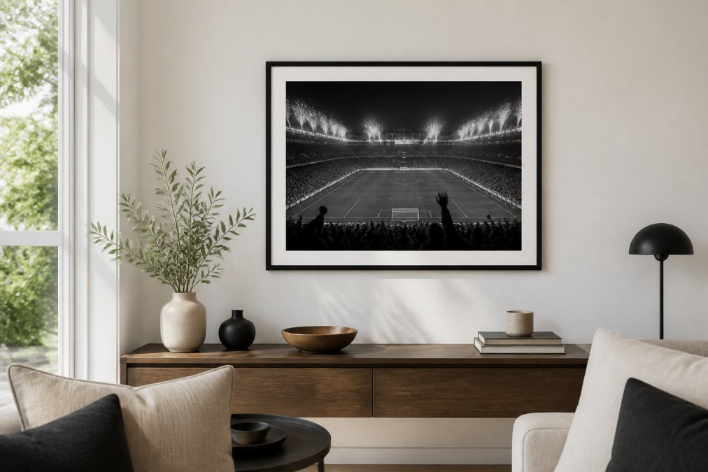 A bright living room wall featuring a framed black-and-white stadium photograph above a wooden console table, with natural light coming from a nearby window